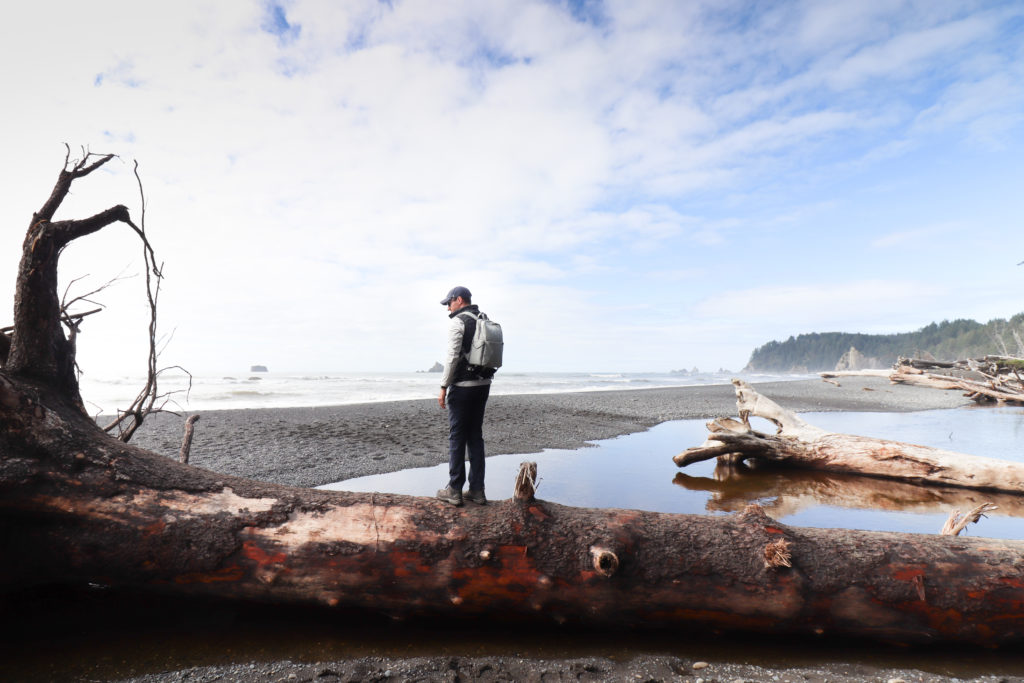 Man standing on driftwood log on Rialto Beach