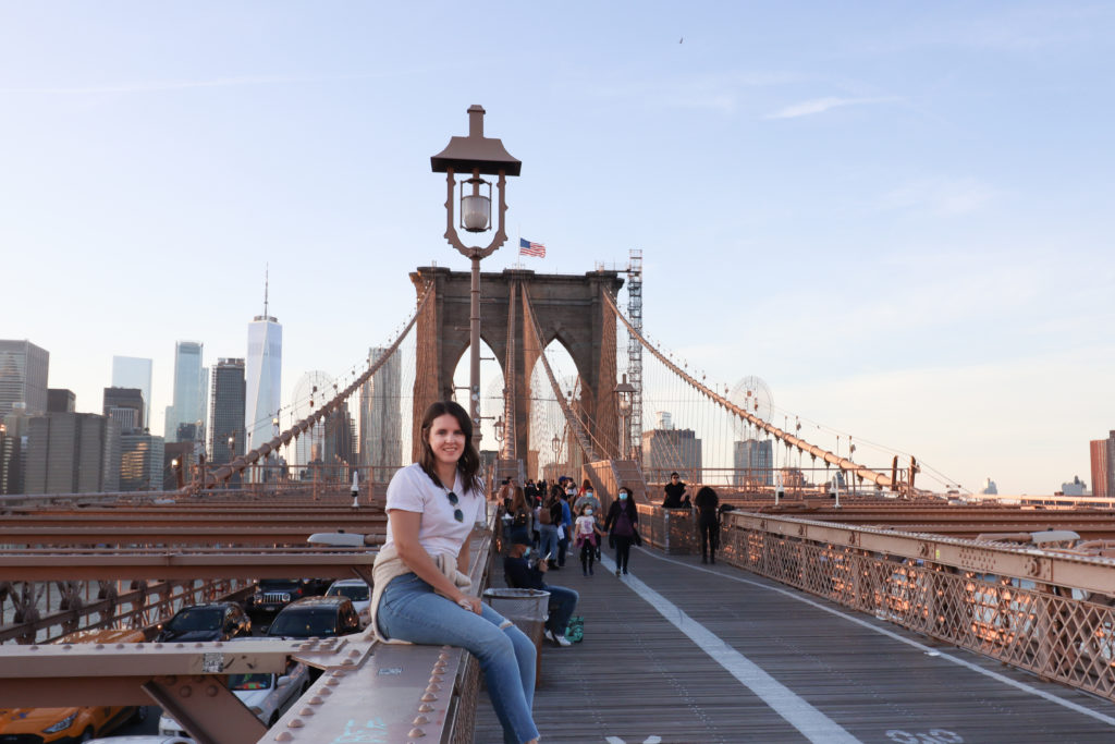 Women sitting on the Brooklyn Bridge with the Manhattan skyline in the background.