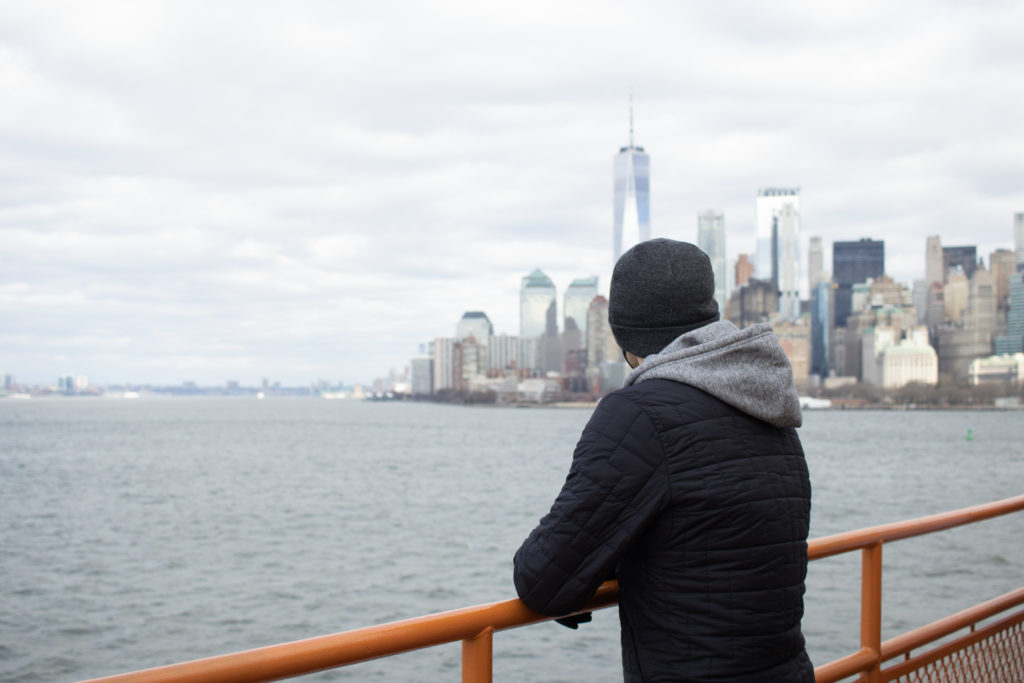A man standing on the Staten Island Ferry with the Manhattan skyline view in the background.