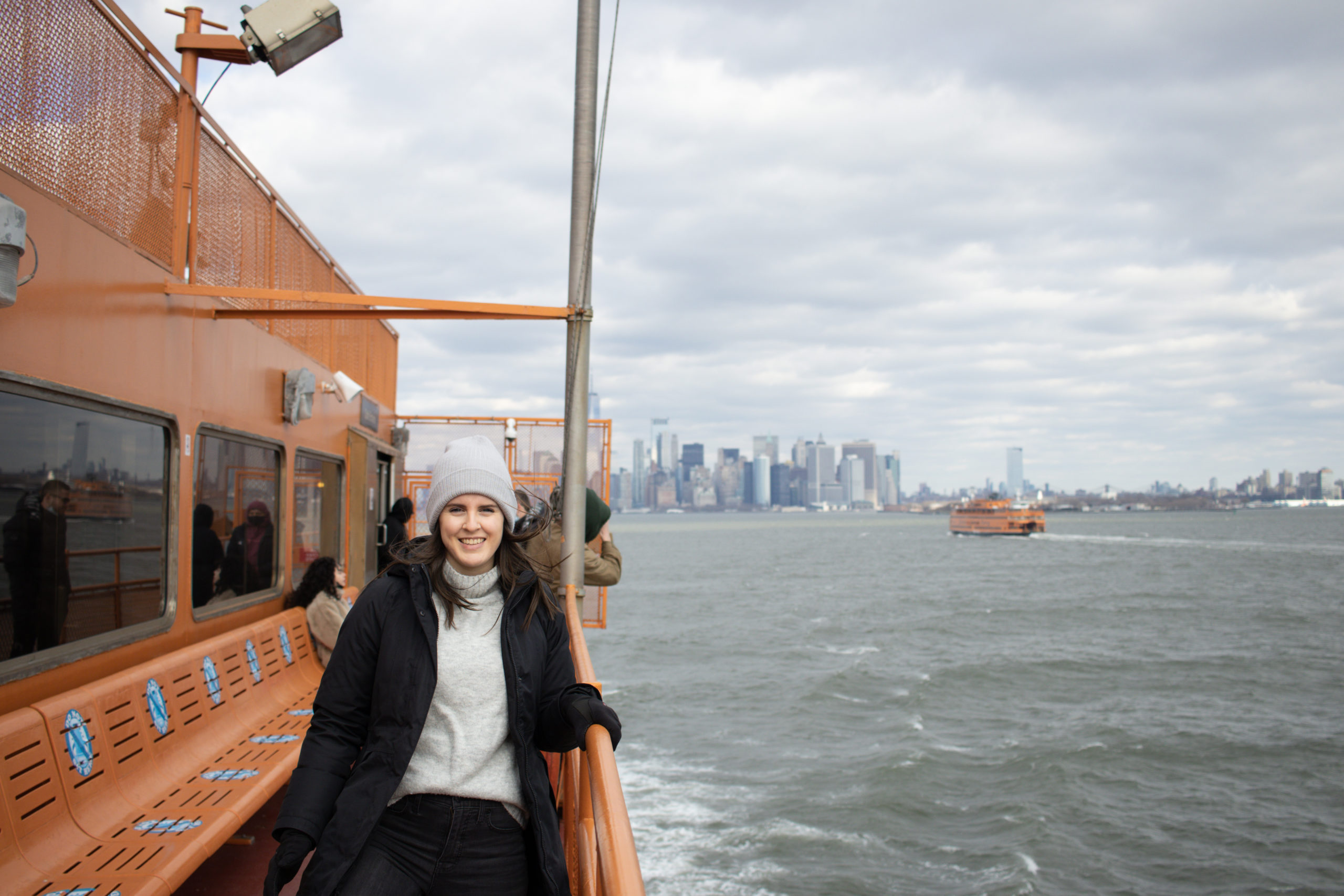 A woman on the Staten Island Ferry with the Manhattan skyline in the background.