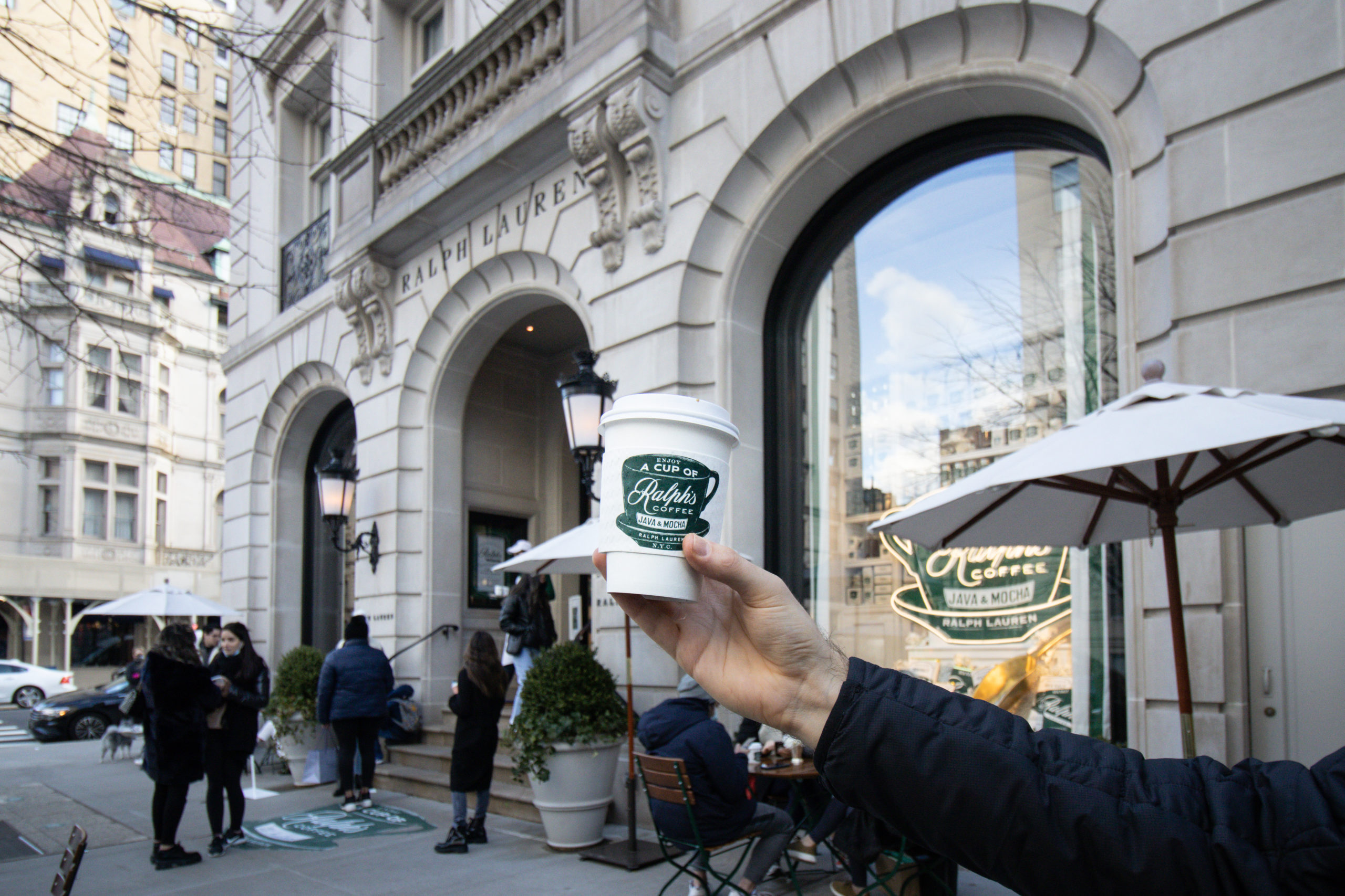A man holding a coffee cup in front of Ralph's, one of the must see NYC coffee shops.