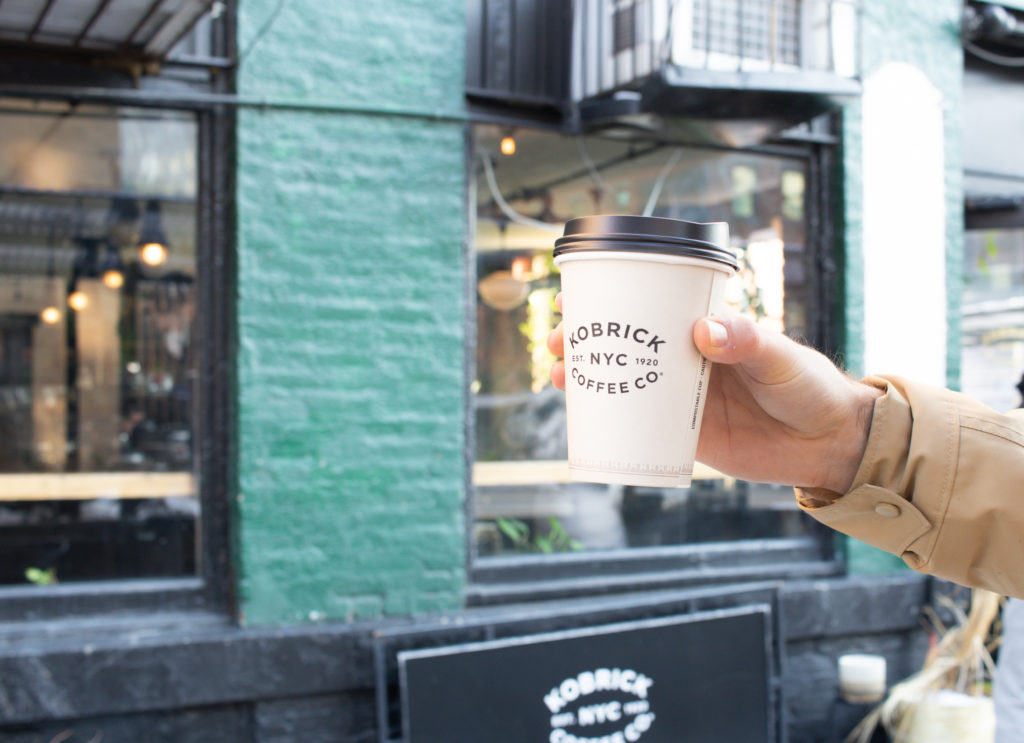 A coffee cup held in front of Kobrick's, one of the best NYC Coffee Shops