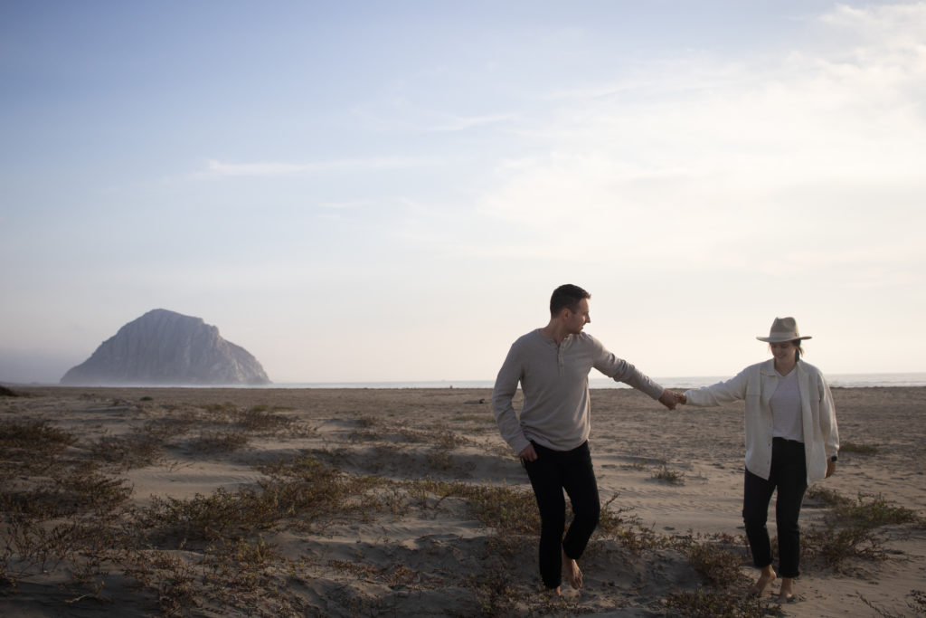 A couple holding hands and walking along Morro Bay beach