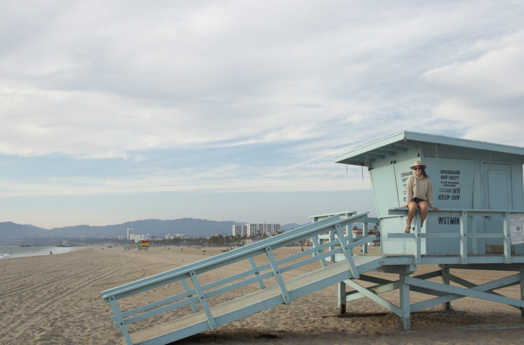 Woman sitting on a beach lifeguard hut, a stop along the Pacific Coast Highway road trip