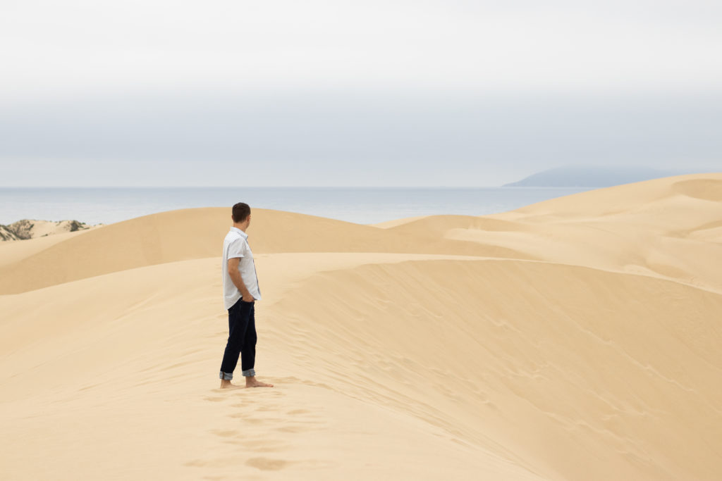 A man standing in Pismo Dunes looking back with the ocean in the far background