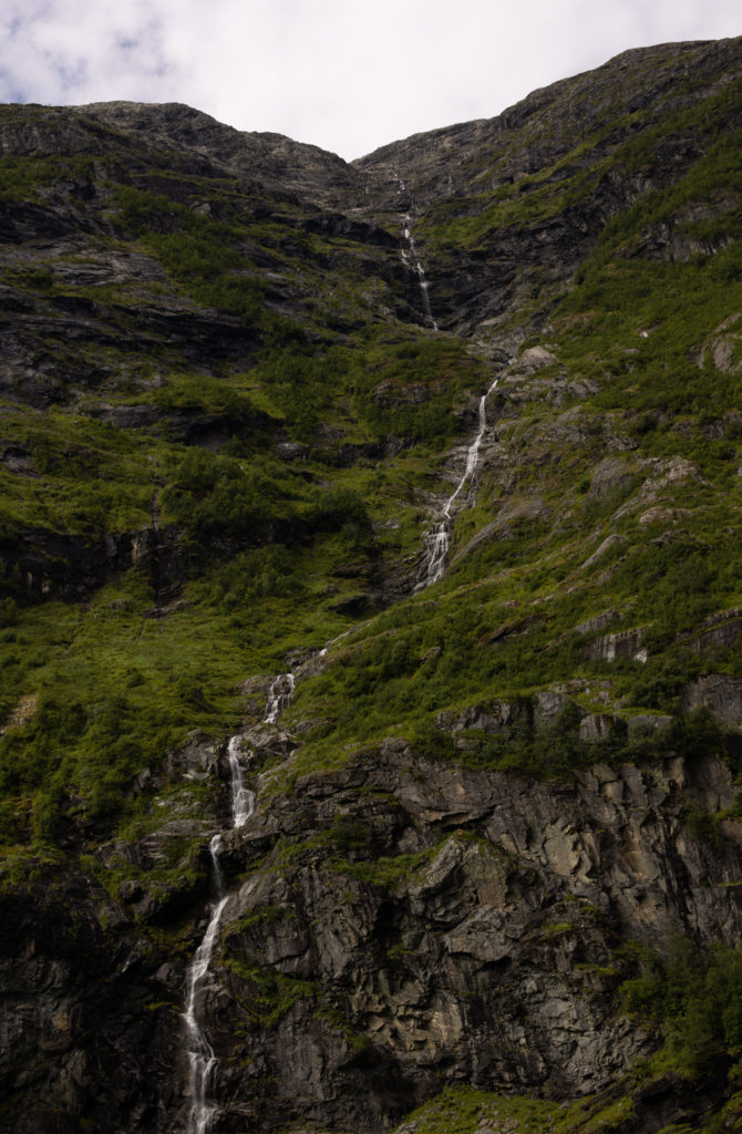 A waterfall cascading down the side of a green mountain in Flåm Norway